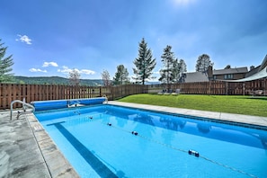 Una piscina rectangular con un cerco de madera y un área verde al fondo.