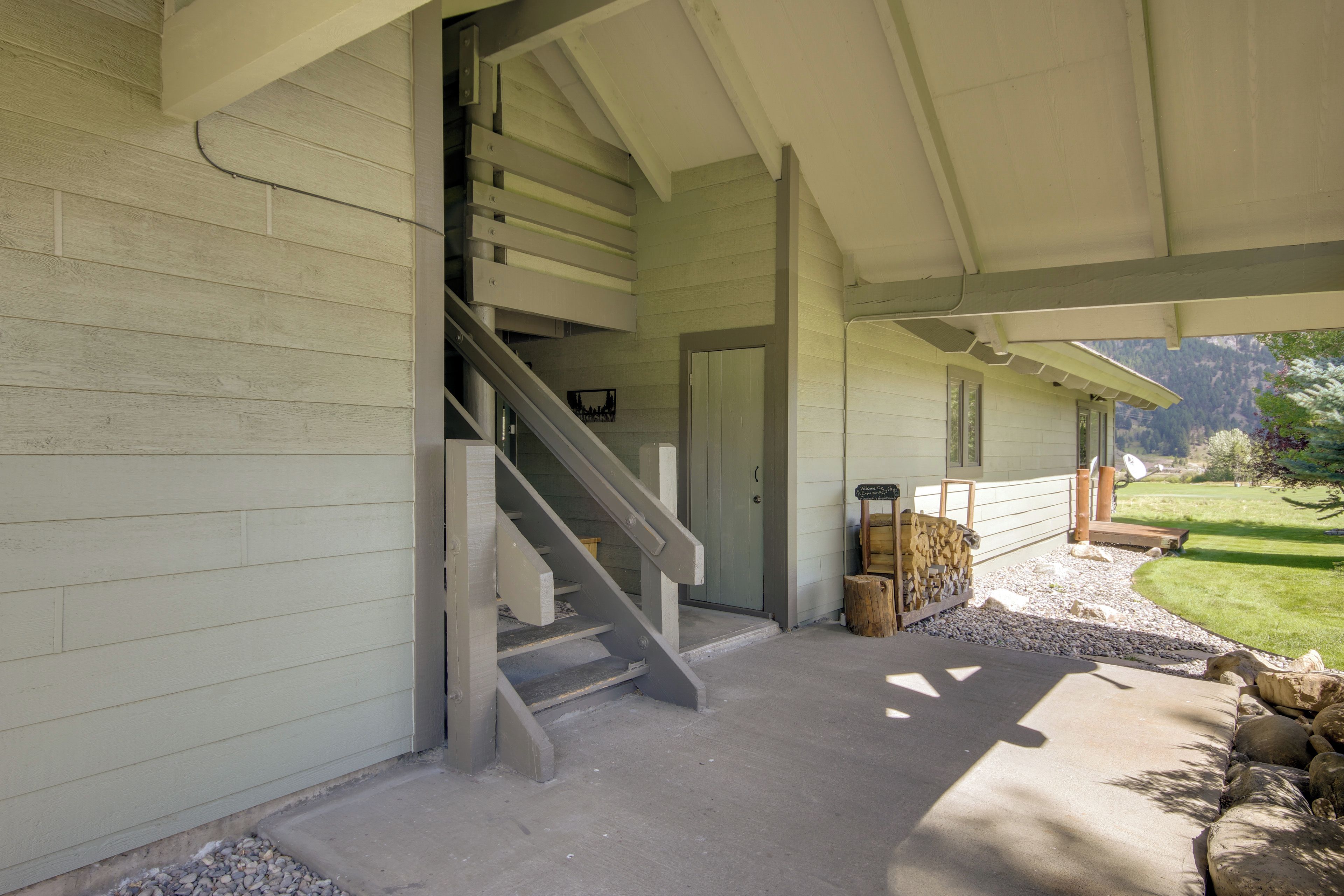 A covered outdoor area with a concrete floor, a wooden staircase, and a view of a green landscape.