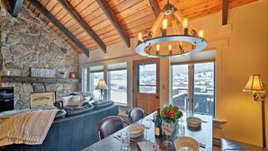 A cozy dining area with a stone wall, wooden ceiling, and a view of a snowy landscape through large windows. - Big Sky Condo w/ Resort Amenities & Mountain Views (Big Sky)