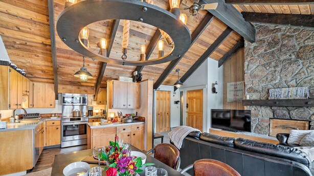 A modern kitchen with wooden cabinets, stainless steel appliances, and a dining area with a table set for four. - Big Sky Condo w/ Resort Amenities & Mountain Views (Big Sky)