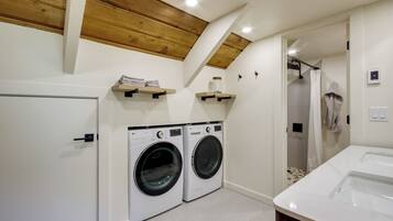 A laundry room with two front-loading washing machines, a wooden ceiling, and a shower area.