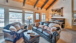 A spacious living room with a high ceiling and large windows, featuring a leather sofa, ottoman, and a dining area. - Big Sky Condo w/ Resort Amenities & Mountain Views (Big Sky)