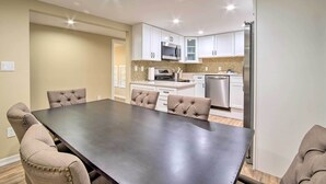 Une cuisine moderne avec des meubles blancs, des appareils en acier inoxydable et un coin repas comprenant une grande table et des chaises à capitonnage.