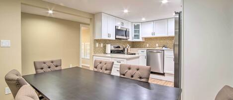 A modern kitchen with white cabinets, stainless steel appliances, and a dining area with a large table and tufted chairs.