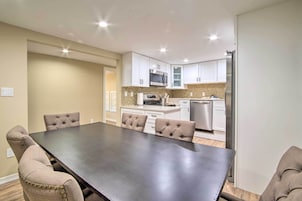 Una cocina moderna con armarios blancos, electrodomésticos de acero inoxidable y un comedor con una mesa grande y sillas capitonadas.