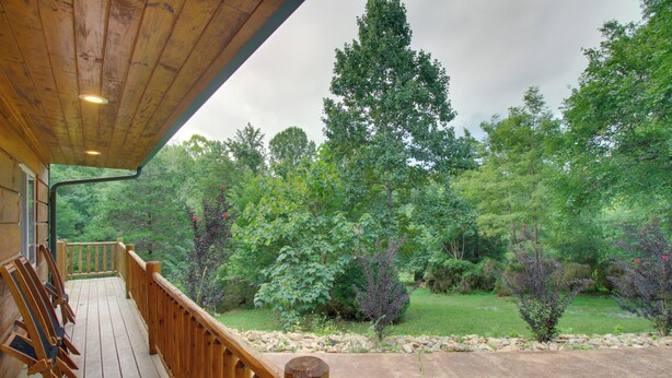 A wooden deck with chairs, overlooking a lush green landscape with trees and a stone pathway.