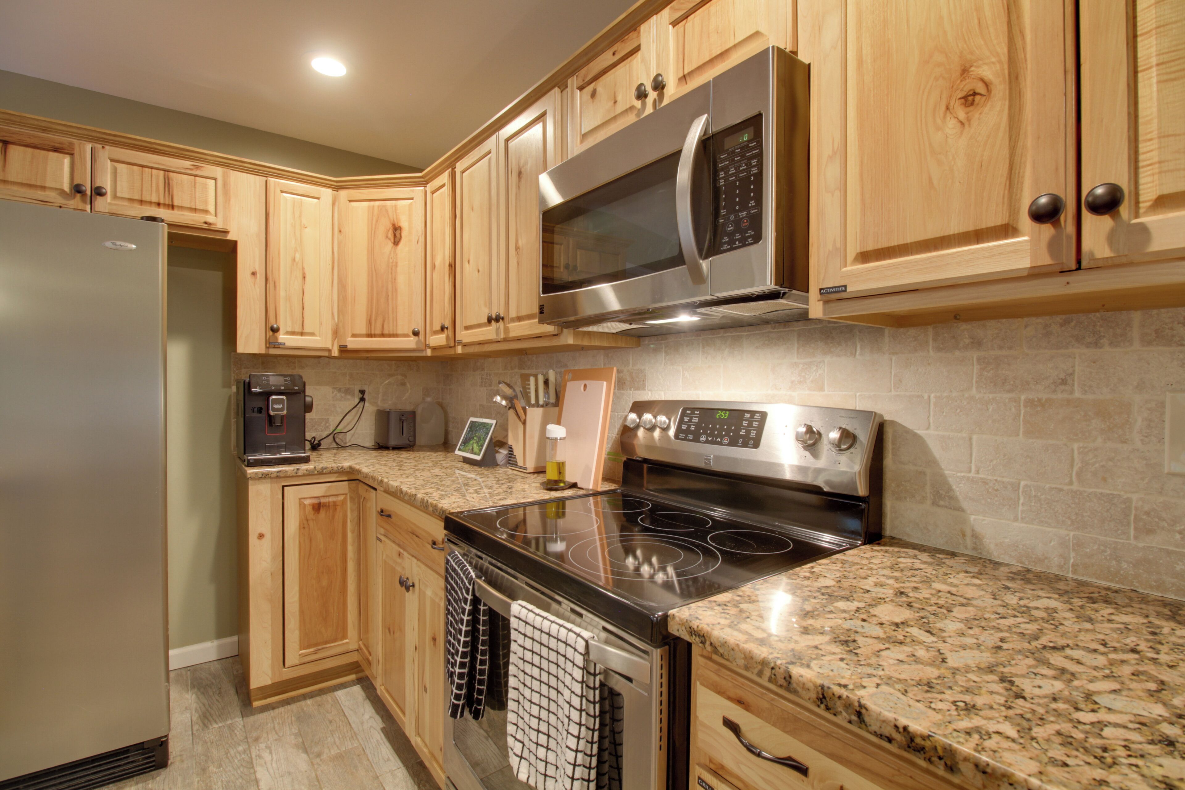 A kitchen with wooden cabinets, a stainless steel refrigerator, a microwave, an oven, and granite countertops.