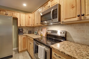 A kitchen with wooden cabinets, a stainless steel refrigerator, a microwave, an oven, and granite countertops.