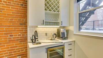 A kitchen with white cabinets, a brick wall, a window, and a dishwasher.
