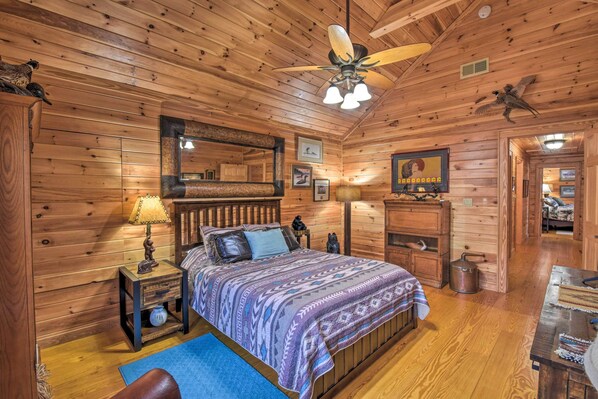 A wooden cabin bedroom with a bed, nightstand, lamp, and ceiling fan. - Dream Catcher: Luxe Cabin w/ Large Deck + Mtn View (Sapphire)