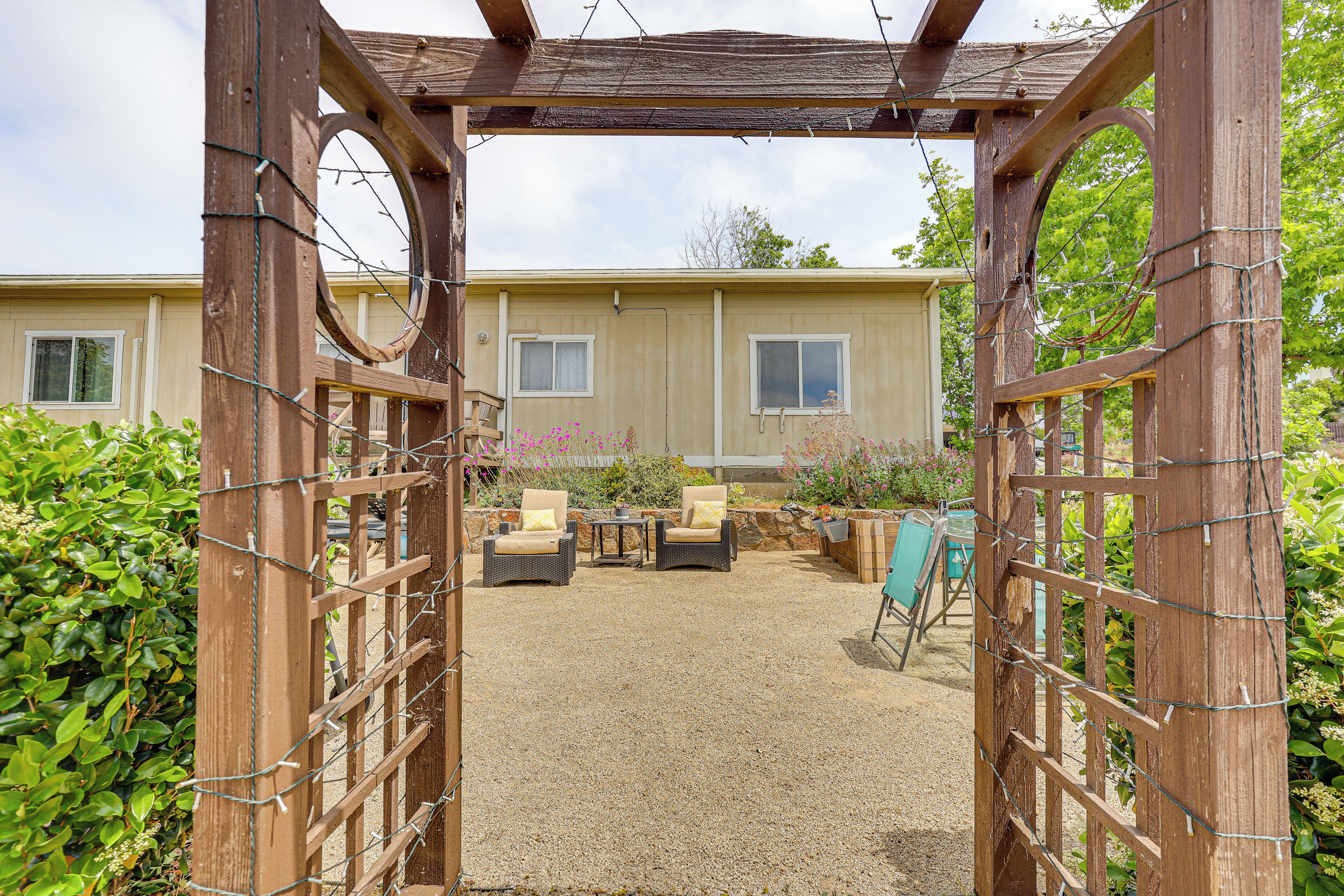 A wooden pergola structure with a gravel patio, two wicker chairs, and a small table.