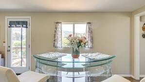 Ein Zimmer mit Glastisch, zwei Stühlen, einer Blumenvase und einem Fenster mit Vorhängen.