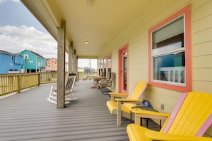 Área externa coberta com deck de madeira, cadeiras Adirondack amarelas e vista para casas coloridas ao fundo.