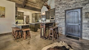 A rustic kitchen with wooden beams, a stone wall, and a deer head mounted above the counter. - Custom Angel Fire Home: Views, Hot Tub & Fire Pit! (Angel Fire)