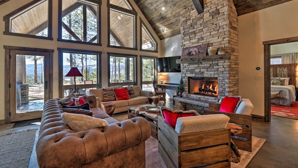 A spacious living room with a stone fireplace, large windows, and a high ceiling. - Custom Angel Fire Home: Views, Hot Tub & Fire Pit! (Angel Fire)