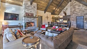 A spacious living room with a stone fireplace, a large leather sofa, and a dining area with wooden furniture. - Custom Angel Fire Home: Views, Hot Tub & Fire Pit! (Angel Fire)