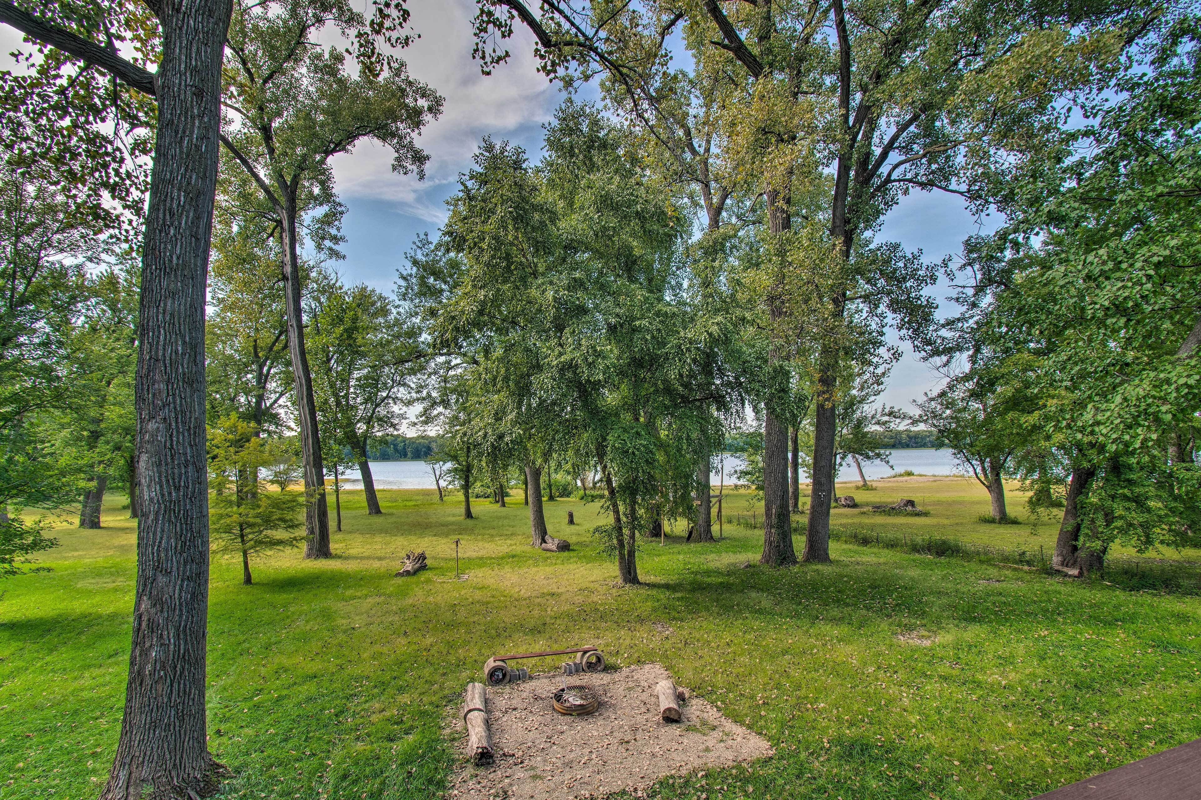 Ein Park mit Feuerstelle, Bäumen und einem See im Hintergrund.