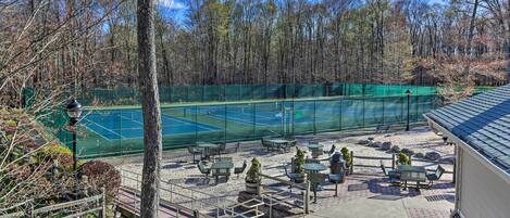A tennis court surrounded by outdoor seating and a forested area.