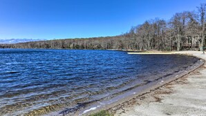 A clear view of a lake with a sandy beach and a forested area in the background. - Walk to Big Bass Lake: Family Home w/ Deck! (Gouldsboro)