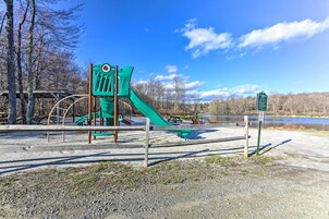 A playground with a slide and climbing structures, surrounded by a gravel area and a body of water in the background.