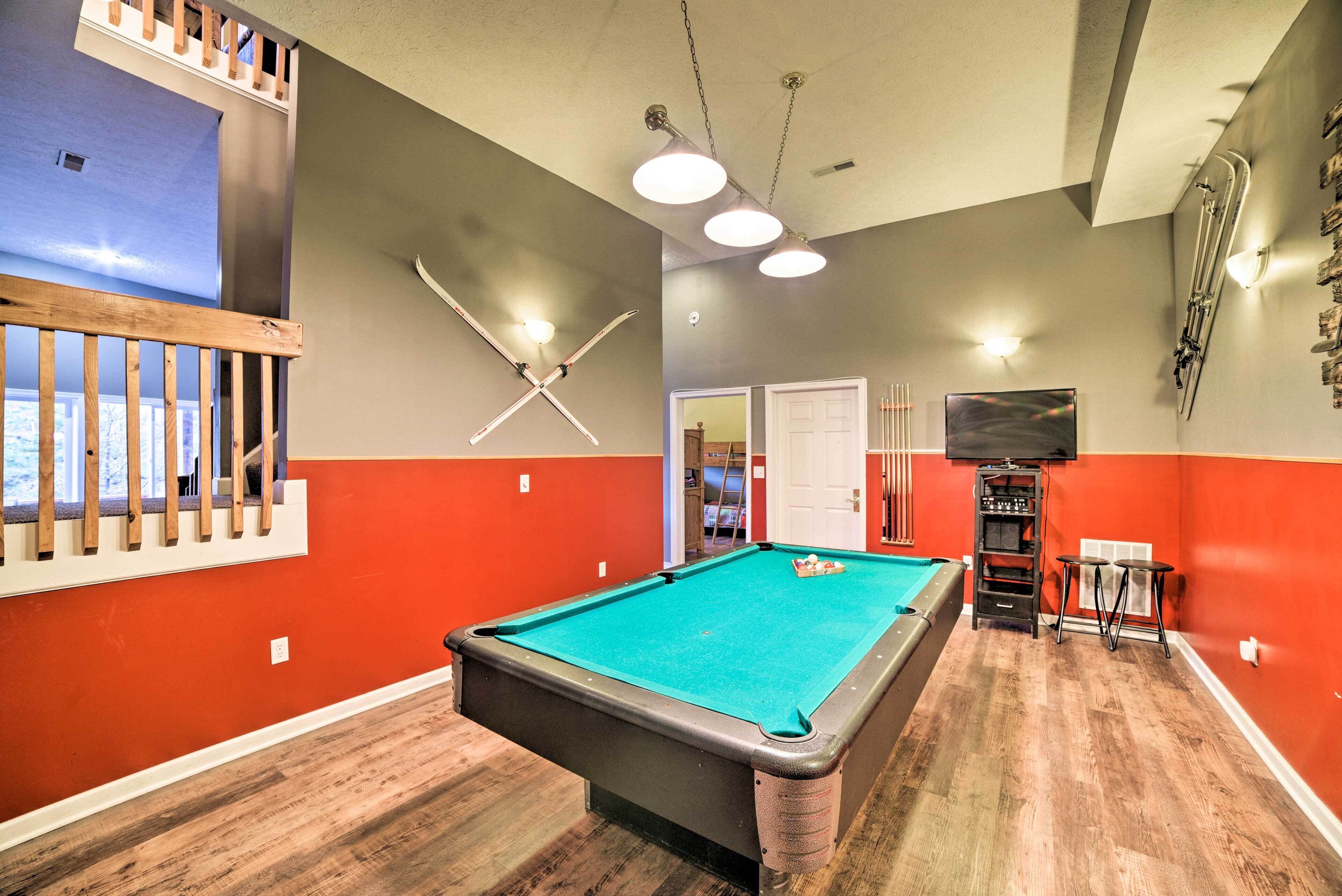 Une table de billard dans une pièce aux murs rouges et gris, avec un plancher en bois et des luminaires au plafond.
