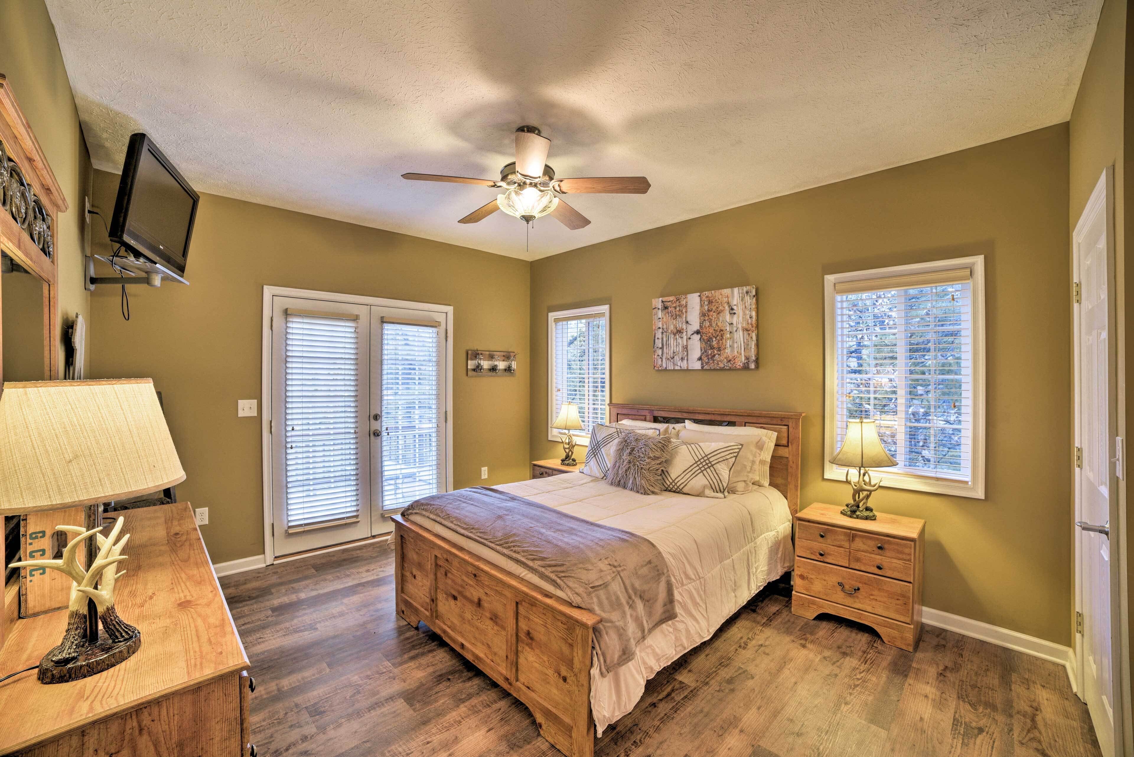 A bedroom with a bed, a nightstand, a dresser, a ceiling fan, and a TV mounted on the wall.