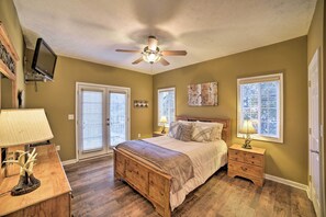 A bedroom with a bed, a nightstand, a dresser, a ceiling fan, and a TV mounted on the wall.