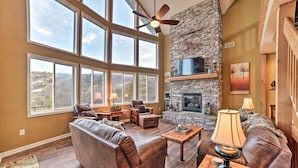 A spacious living room with a stone fireplace, leather sofas, and large windows offering a view of the outdoors.