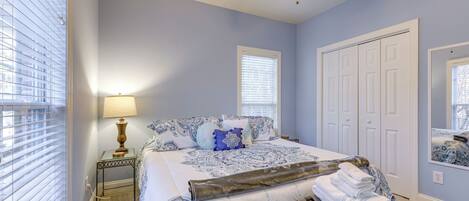 Une chambre à coucher avec un lit, un ventilateur de plafond, une table de chevet avec une lampe et une fenêtre avec des stores.