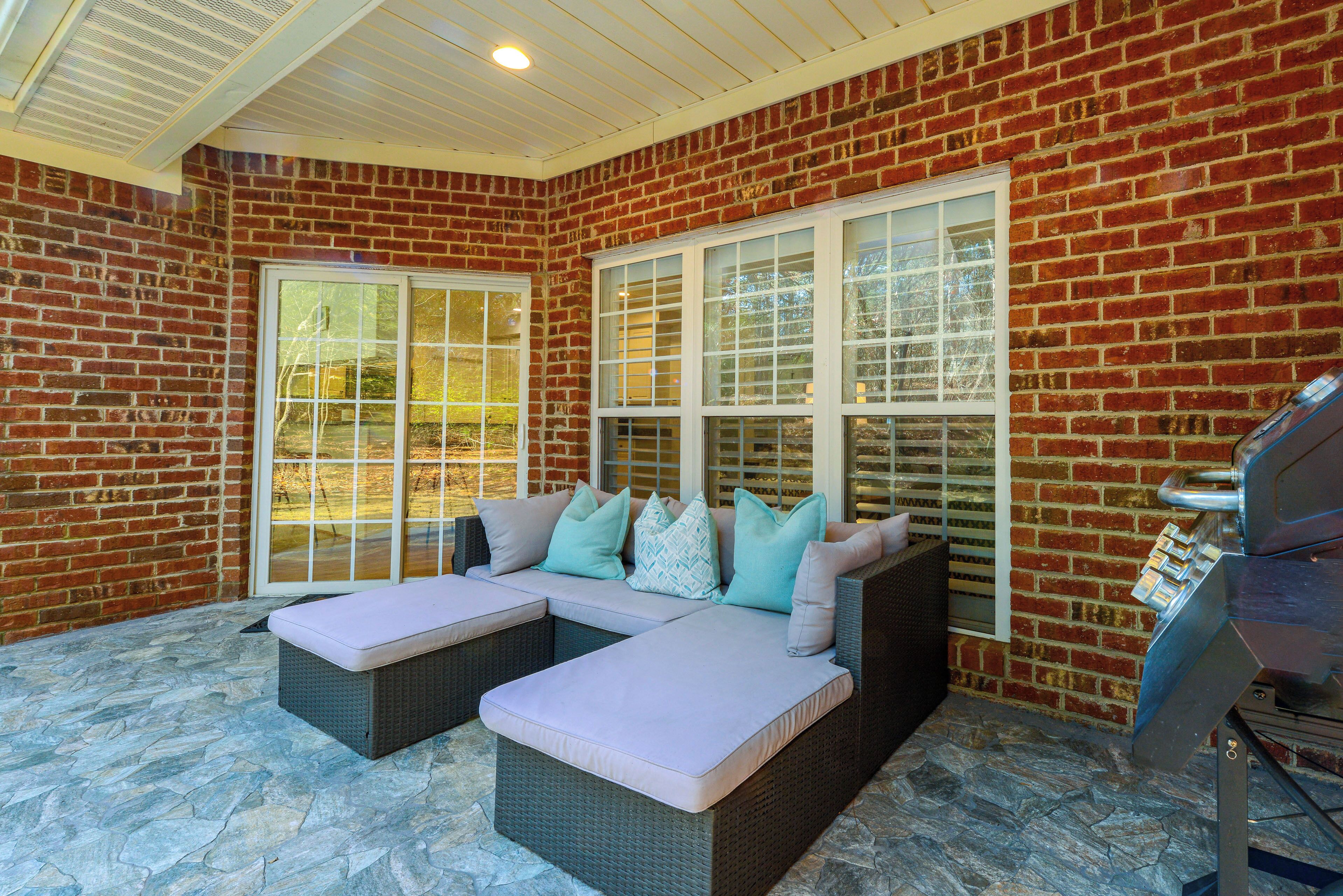 A covered patio area with a brick wall, large windows, and a grill.