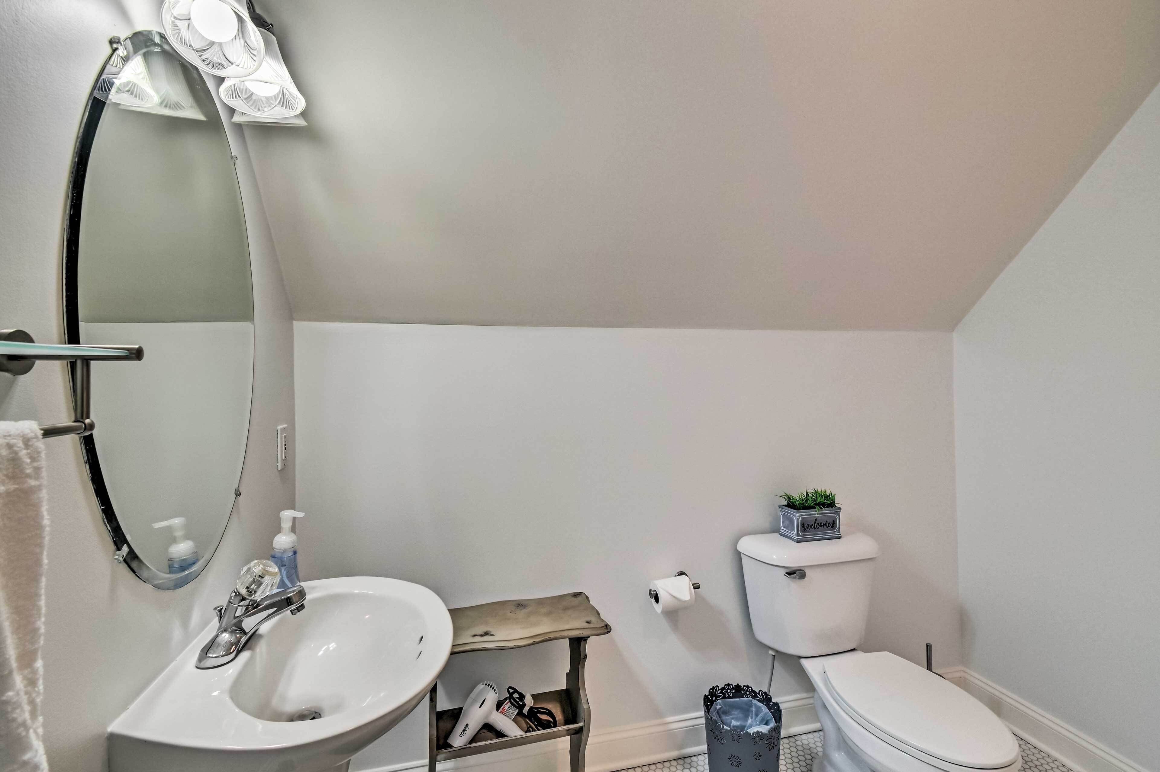 A bathroom with a white sink, mirror, and toilet. There is a small shelf with a plant and a roll of toilet paper.