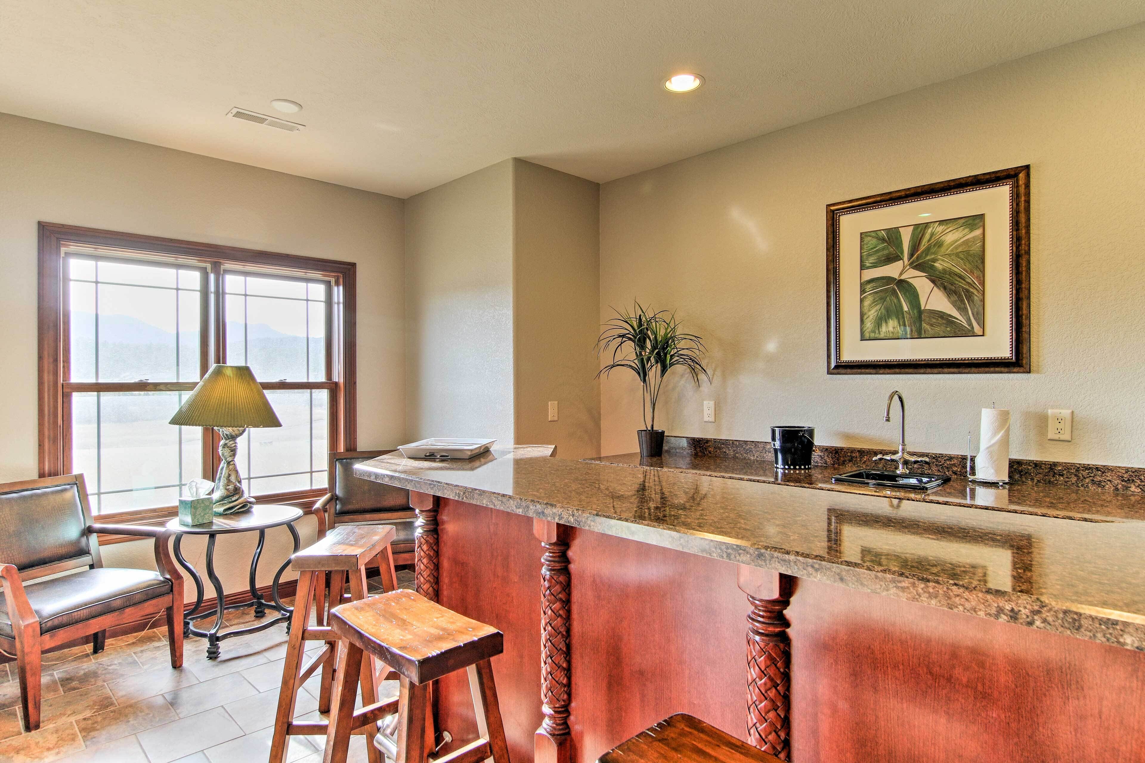 A kitchen with a granite countertop, wooden stools, a table with a lamp, and a window with a view.