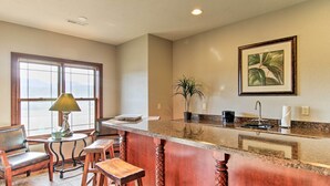 A kitchen with a granite countertop, wooden stools, a table with a lamp, and a window with a view. - Sturgis Vacation Rental w/ Hot Tub & Game Room! (Sturgis)