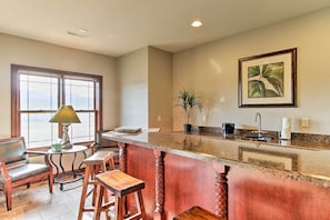 A kitchen with a granite countertop, wooden stools, a table with a lamp, and a window with a view. - Sturgis Vacation Rental w/ Hot Tub & Game Room! (Sturgis)
