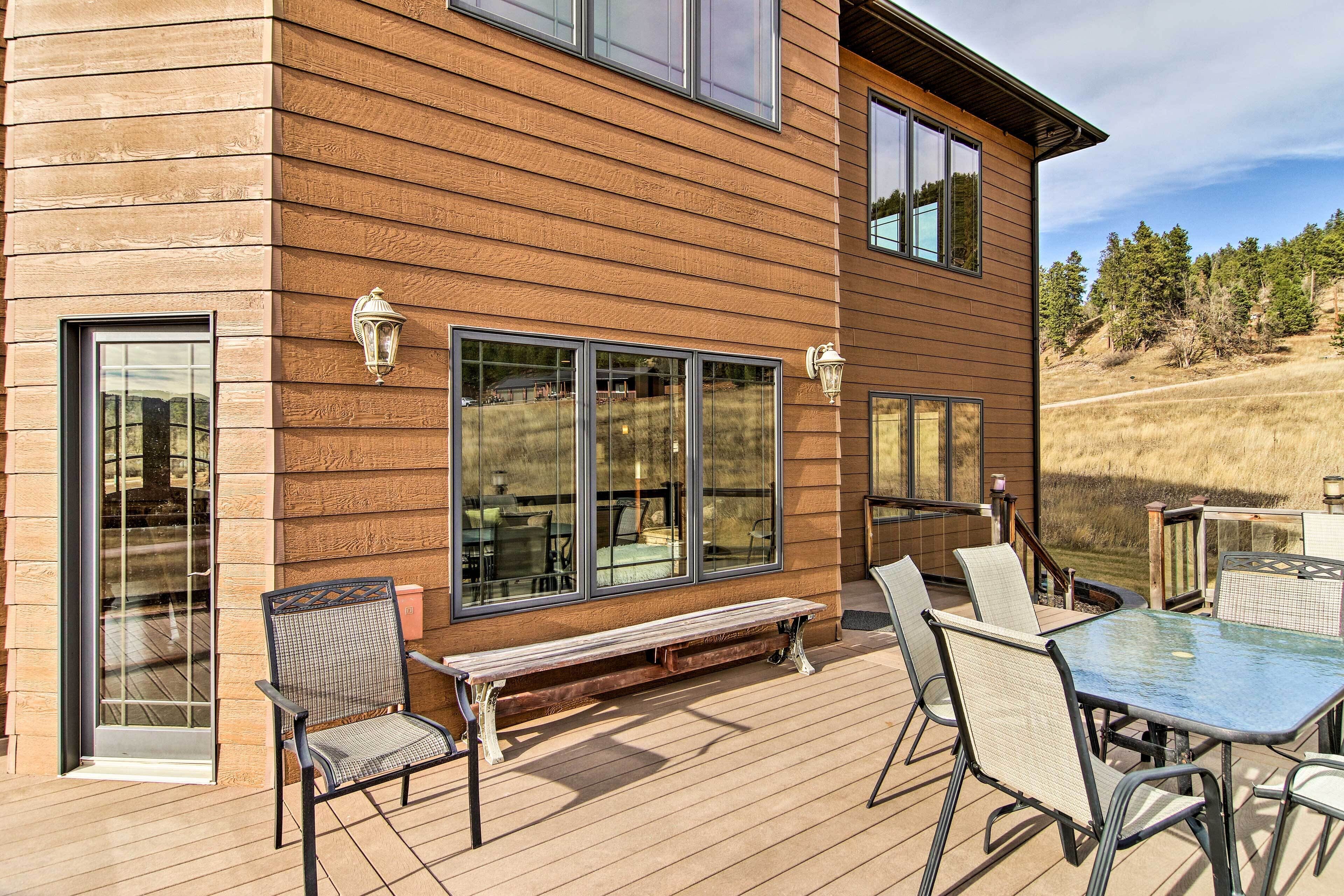 Une terrasse en bois, aménagée avec du mobilier d’extérieur, notamment un banc et des chaises, ainsi qu’une table en verre.
