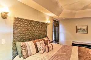 A neatly made bed with multiple pillows and a headboard, a wall-mounted light fixture, and a framed picture on the wall. - Hot Tub, Game Room! Black Hills Rally-ready Estate (Sturgis)