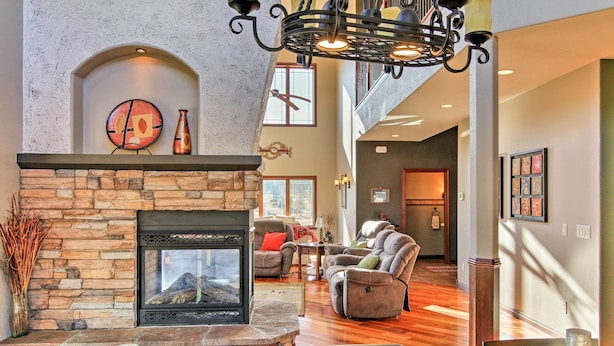 A spacious living area with a stone fireplace, comfortable seating, and a high ceiling with a chandelier.
