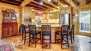 A wooden cabin interior with a kitchen featuring a refrigerator, microwave, and bar stools. - Hike, Fish & Golf: Burnsville Retreat w/ Deck! (Burnsville)