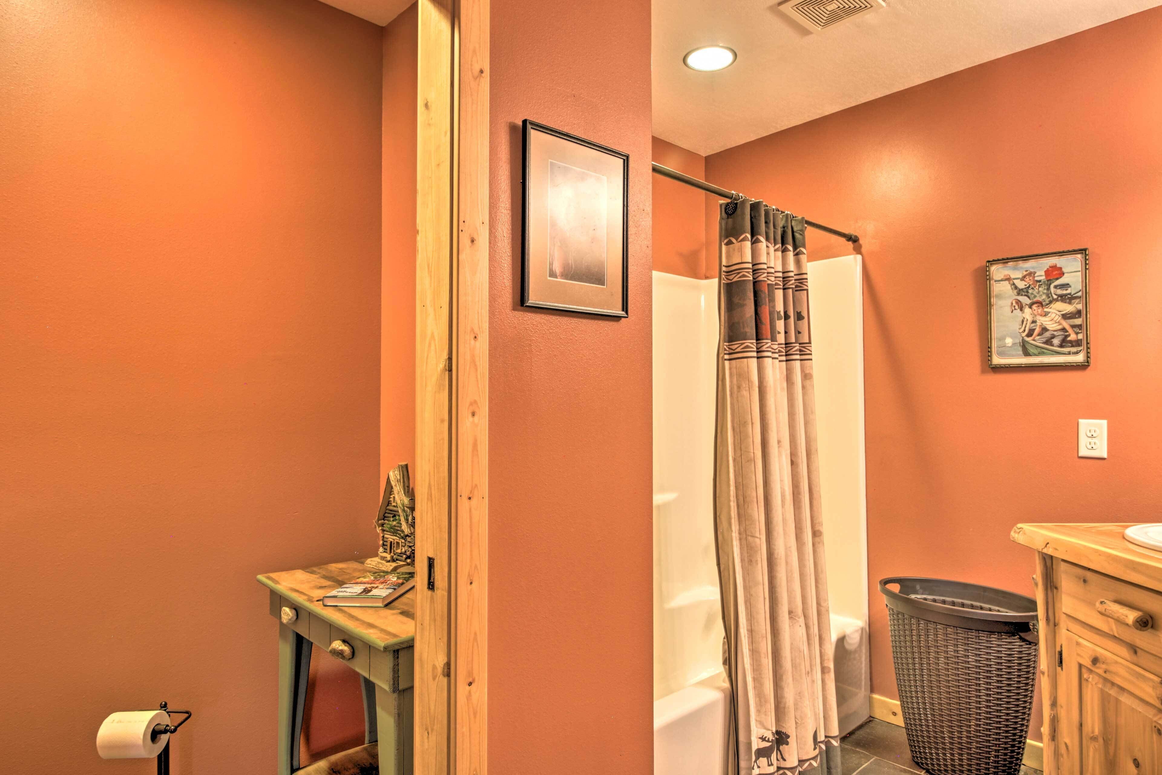 Un baño con tocador de madera, cortina de ducha, cubo de basura y un cuadro en la pared.