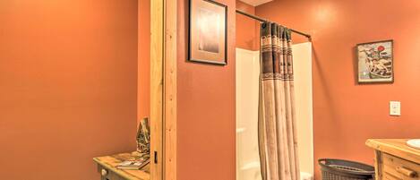 Un baño con tocador de madera, cortina de ducha, cubo de basura y un cuadro en la pared.