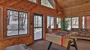 A cozy room with wooden walls, large windows, a foosball table, and a mounted deer head. - Dock, Fire Pit & Beach! Expansive Ruth Lake Home (Emily)