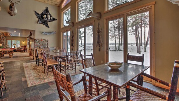 A spacious dining area with large windows, wooden furniture, and various mounted animal heads on the walls. - Dock, Fire Pit & Beach! Expansive Ruth Lake Home (Emily)