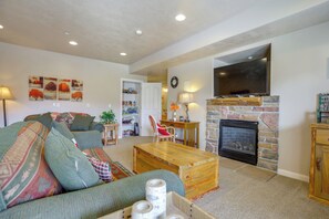 A living room with a stone fireplace, a television mounted above it, and a sofa with patterned cushions. - High-end Huntsville Condo w/ Private Hot Tub! (Huntsville)