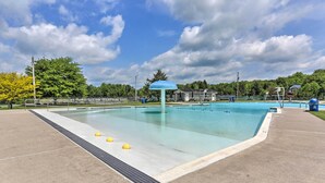 Une piscine dotée d’un auvent bleu, entourée d’une zone délimitée par une clôture et d’arbres.