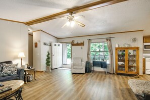 Un salon spacieux doté de planchers en bois franc, d’un ventilateur de plafond, d’un canapé, d’une table basse et d’un meuble contenant de la verrerie.