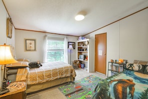 A bedroom with a bed, a desk, a lamp, a bookshelf, and a door. - Haven in the Woods w/ 150 Acres, 2 Ponds (Brownstown)