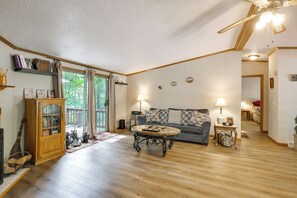 Un salon avec un plancher en bois, un canapé, une table basse, une bibliothèque et un ventilateur de plafond.