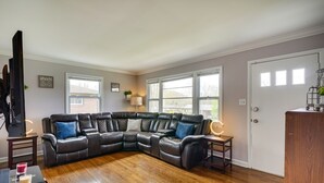 A living room with a sectional sofa, a television, a small table with candles, and a door with windows. - Home Rental w/ Yard Near Downtown Greensboro! (Greensboro)