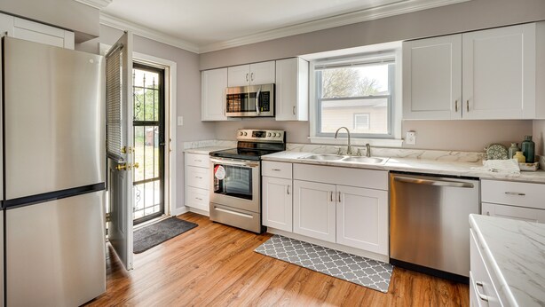 A modern kitchen with white cabinets, stainless steel appliances, and a wooden floor. - Home Rental w/ Yard Near Downtown Greensboro! (Greensboro)