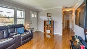 A spacious living room with a leather sofa, a wooden bookshelf, and a hallway leading to another room. - Home Rental w/ Yard Near Downtown Greensboro! (Greensboro)